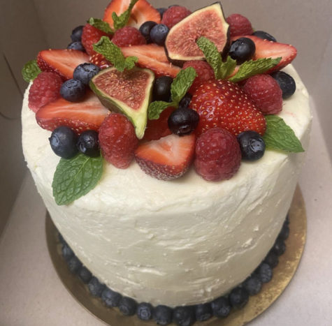 Pictured is a chocolate cake with vanilla buttercream, topped with berries, figs, and mint.
