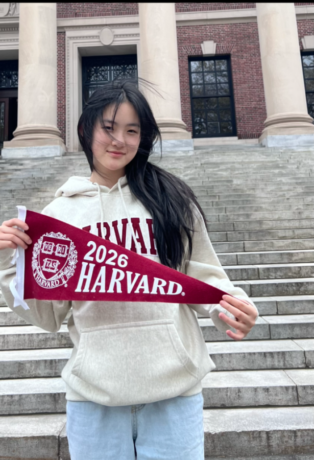Stuyvesant High School senior Michelle Zhang 22 poses outside of Harvard University with a Harvard banner during the 2026 Accepted Students Meeetup.
