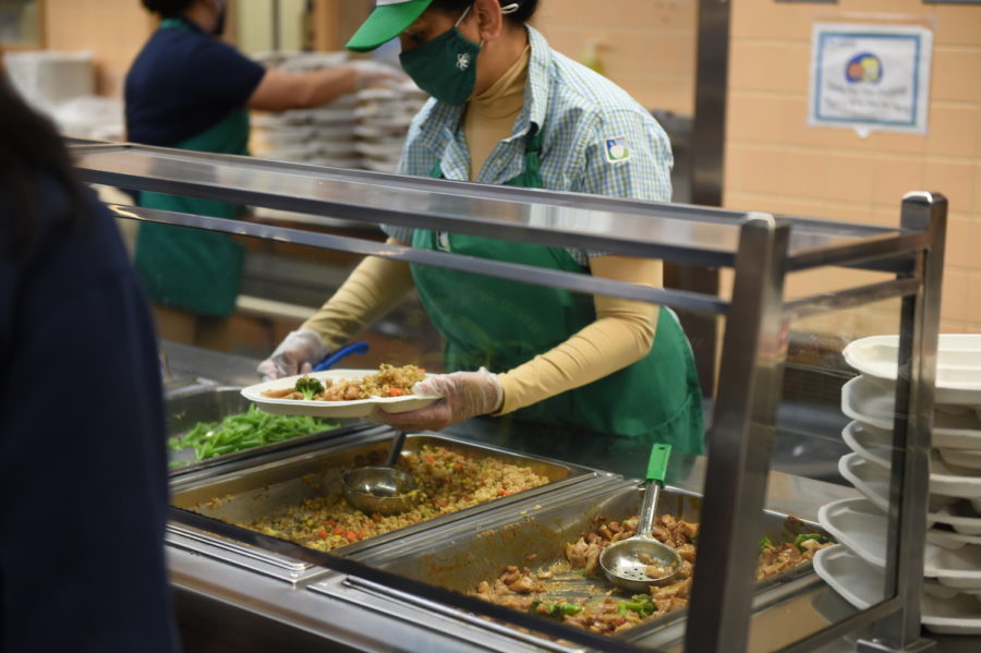 Behind the food trays, a lunch aide serves students stewed chicken and broccoli with fried rice and green beans as sides. She always delivers a cheery greeting. 