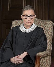 Ruth Bader Ginsburg (RBG) wearing one of her many famous collars made out of beads from South Africa. RBG was known as a trendsetter in Supreme Court fashion as she wore unique collars with her classic black robe.
