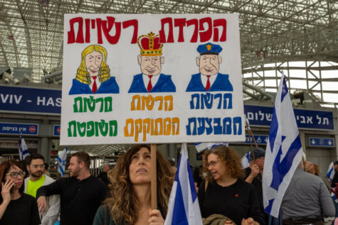 A protester on March 23, 2023 with a sign entitled “Separation of Powers.” It depicts Netanyahu as a judge, police officer, and  king, with power over each branch of the Israeli government.
