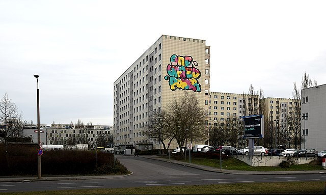 This is an apartment building in Berlin with 1UP’s signature “One United Power” phrase painted onto one of the blank walls of the structure. (Photo Credit: Singlespeedfahrer, CC0, via Wikimedia Commons)