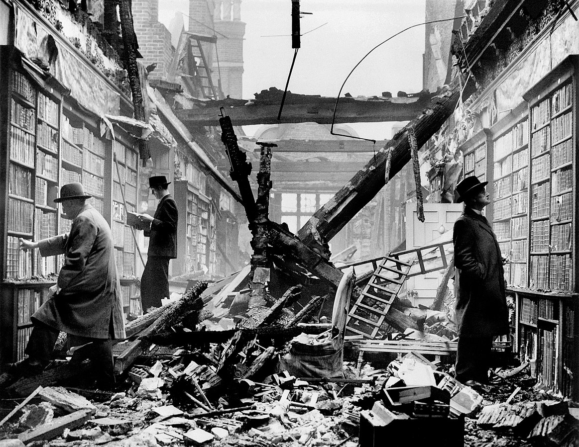  Three men in the Holland house view the remains of the library after it had been burned down during the 1940 London air raids. It demostrates “the lengths people will go to to keep reading,” noted Dr. Adam Tramantano, an English teacher at the Bronx High School of Science. Photo Credit: Harrison for Fox Photos Limited[1] (collection later acquired by Hulton Archive, subsequently purchased by Getty Images[2]). Image was first released Crown Copyright by Press and Censorship Bureau of en:Ministry of Information (United Kingdom).[2], Public domain, via Wikimedia Commons