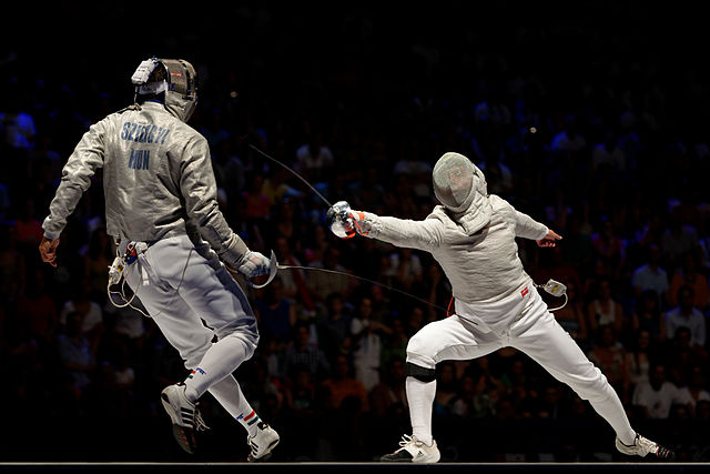 Pictured is Áron Szilágyi (at left) against Nikolay Kovalev (at right) during the Semi-Finals for the 2013 Budapest World Fencing Championship. 
(Photo Credit: © Marie-Lan Nguyen / Wikimedia Commons)