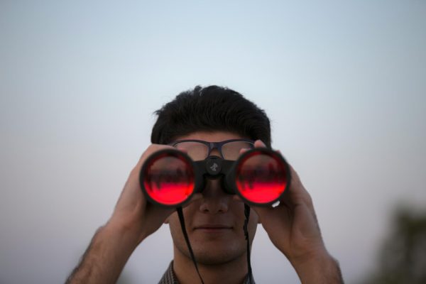 The subject is holding binoculars, symbolizing ‘looking deeper’ into a person, a conversation, and/or an action. It is the act of observing, and being able to understand someone even if they don’t say a word. (Photo Credit: Mostafa Meraji / Unsplash)