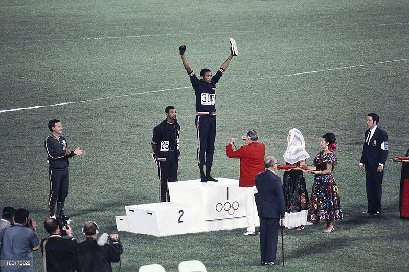 The Olympic Games have long been intertwined with athlete protests. Tommie Smith, John Carlos, and Peter Norman’s 1968 protest is recognized as one of the first and most groundbreaking demonstrations in Olympic history. [Photo Credit: Angelo Cozzi (Mondadori Publishers), Public domain, via Wikimedia Commons]