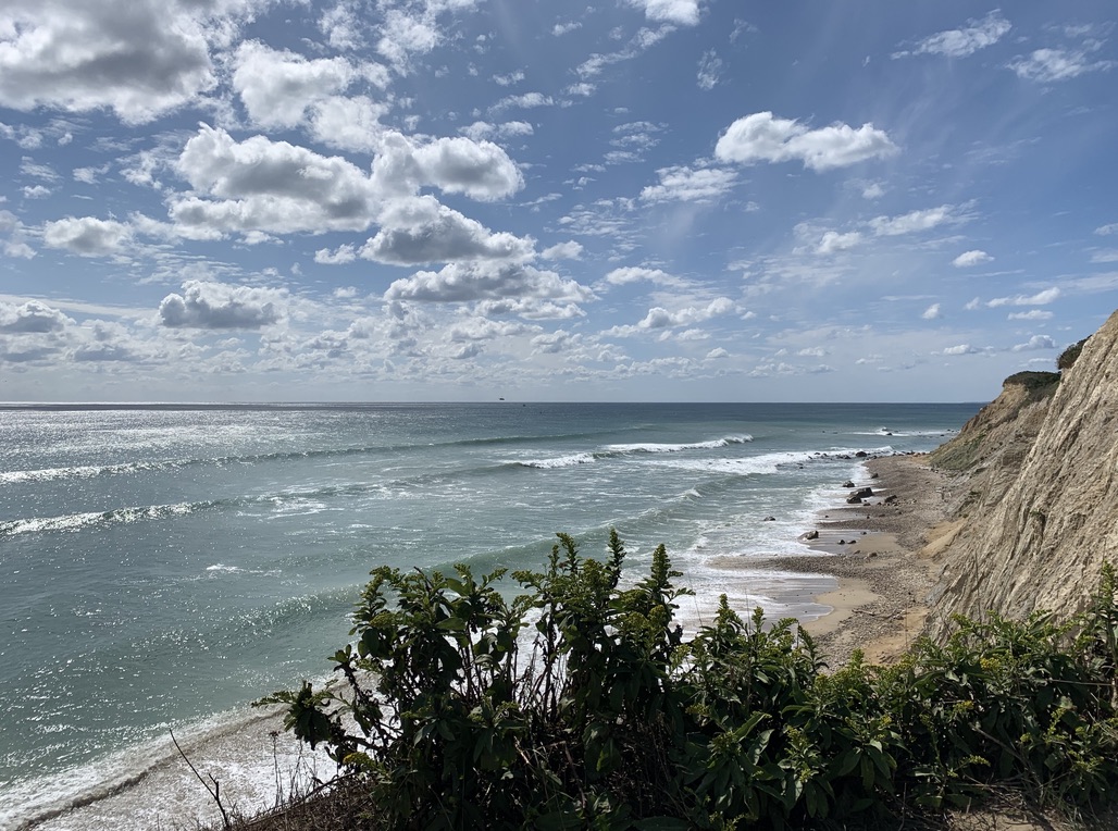 Pictured is a bright, sunny day on Block Island. This photo was taken from an angle above, capturing the edge of the Mohegan Bluffs and offering a scenic view of the ocean waves. 
