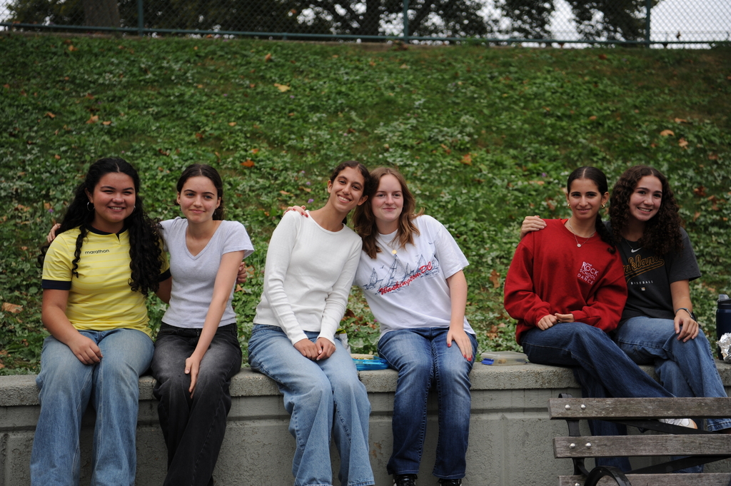 Six Bronx Science students sit together in the front campus courtyard. Their body language of shoulders touching and arms wrapped around each other indicates their closeness and their bond.