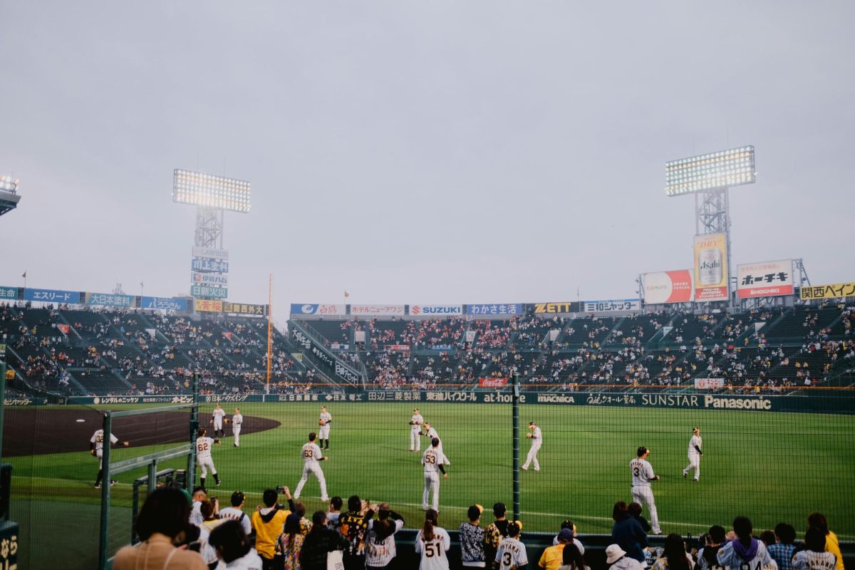 Pictured is a game at Koshien. Many people can be seen standing right up against the fence in school colors, eager to watch the game play out. (Photo Credit: Ayyeee Ayyeee / Pexels)