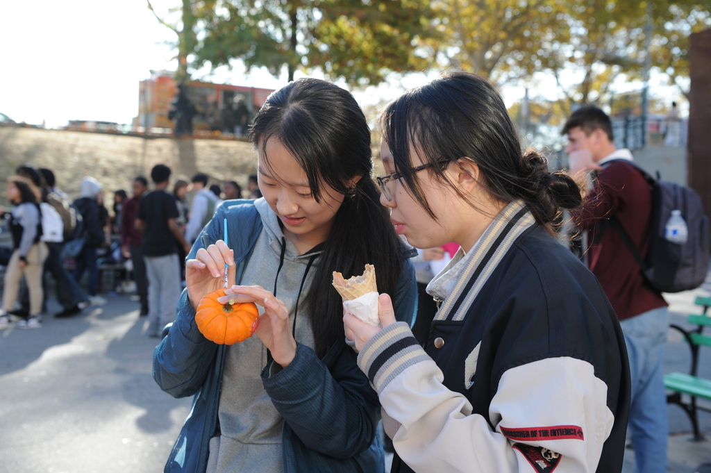 A student looks on as her friend decorates a pumpkin.
