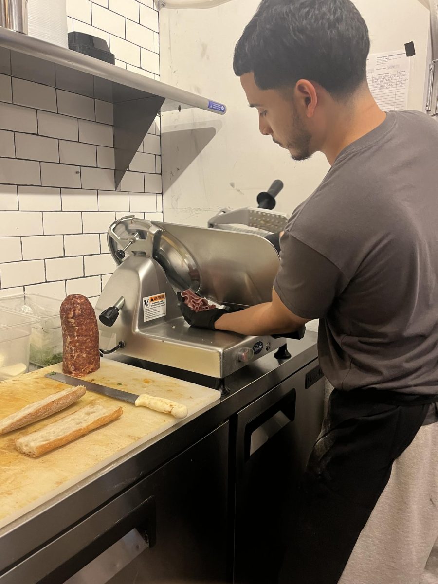 Here is a snapshot of Andrew Vazquez slicing meat for a sandwich, in Regina's Upper East Side Grocery.