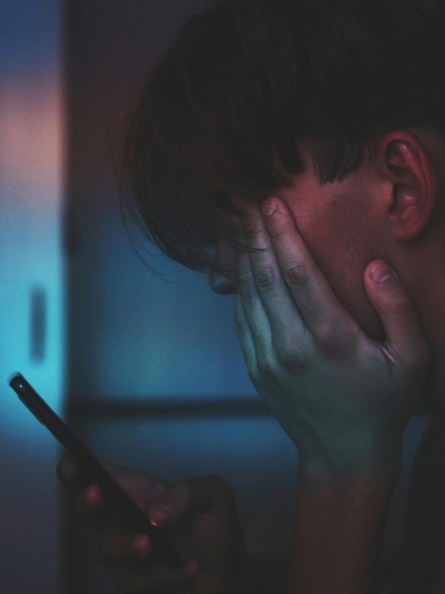 This photograph is a depiction of a gloomy young man scrolling through his phone in the dark, a scene seen by many across the globe. (Photo Credit: Adrian Swancar / Unsplash)