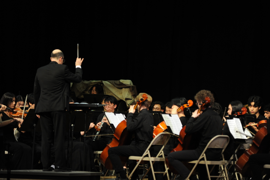 Mr. Paul DeSilva conducts the orchestra from the front of the stage. 