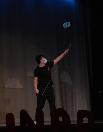 During the annual showcase, a student uses a string stretched between two sticks to skillfully toss a blue yoyo into the air. 