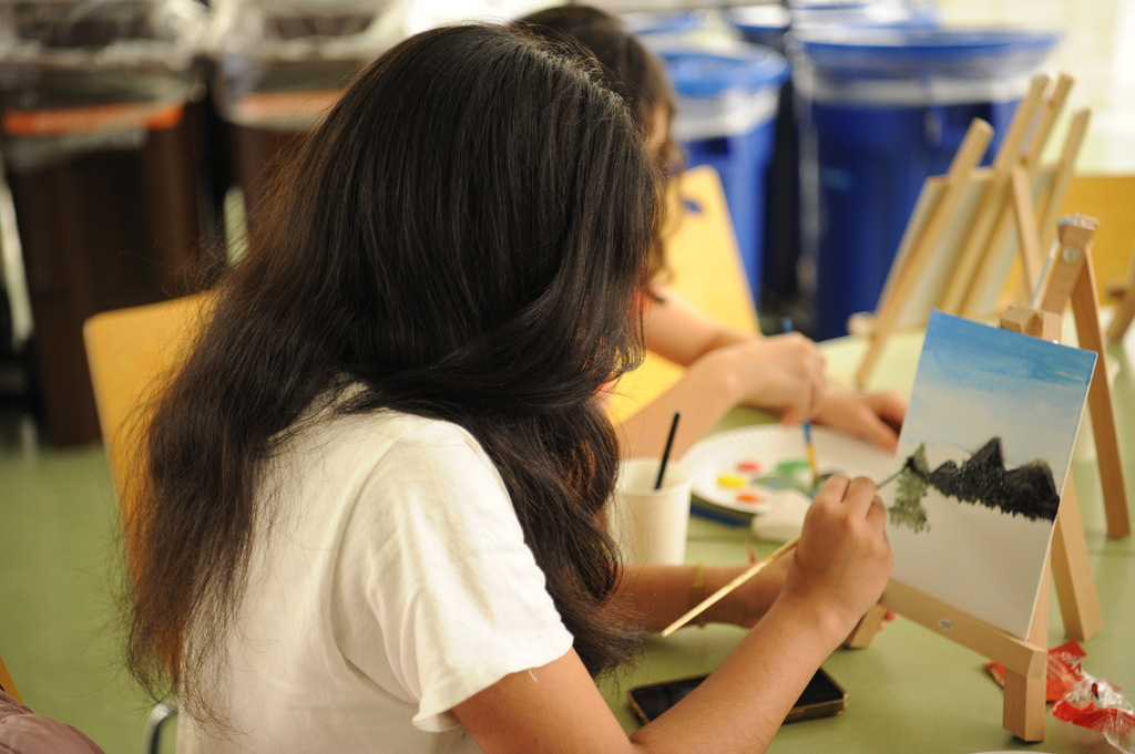 A student flawlessly paints a mountain landscape and tall trees with a skilled hand.